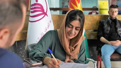 An Iraqi woman signs administrative documents on a desk to open her own business