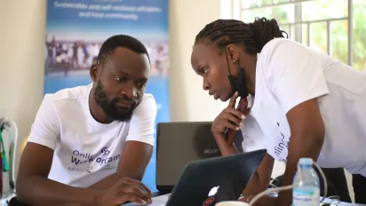 A woman speaks to a man in front of a computer in a classroom setting