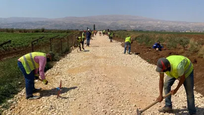 Several men wearing yellow vests work to rehabilitate rural road using hand tools