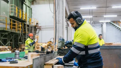 Carpenter wearing safety equipment, assembling wooden pallets in a recycling plant 