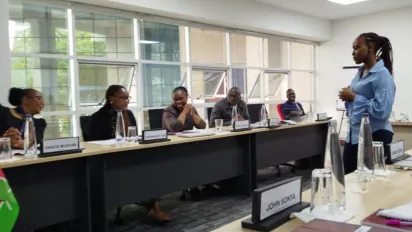 Five persons sitting are being trained by a woman standing up