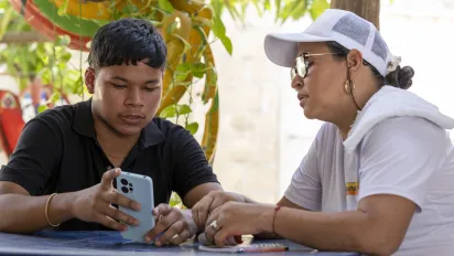 Rafael Meza et sa mère, Marlin Judith, sont assis ensemble à une table. Rafael lui montre son téléphone portable.