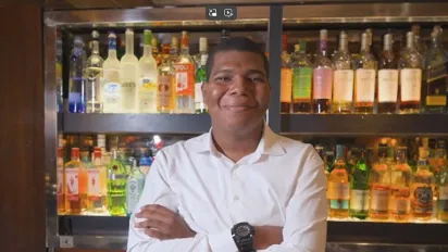 A young employee stands behind the bar counter, smiling