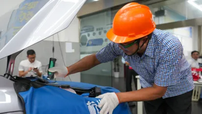 A man wearing an orange hard hat is working on a car engine.