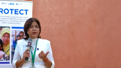 A lady holding a microphone speaks in front of a meeting room. 