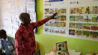 A cocoa farmer stands in front of two posters teaching.