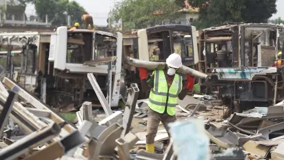 Travailleur transportant une pièce métallique dans un site de démantèlement de véhicules.