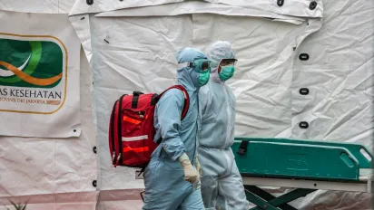 Two workers in full protective gear walking by a tent