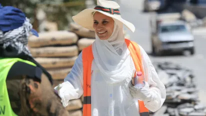 Smiling lady (Alaa Mhairat) wearing hat and fully covered in white clothes and gloves, talking to a worker in street in Jordan