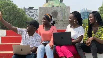 Four friends with laptops smile and take a selfie at a monument in Cotonou, Benin