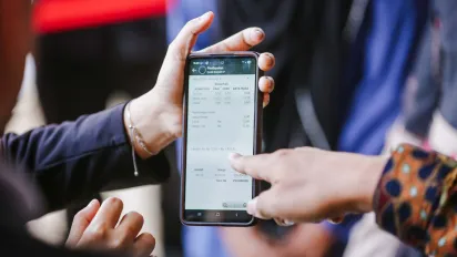 Two people review information on a smartphone displaying a dairy cooperative management application. One person points to production and payment data on the screen, illustrating the use of digital tools to improve record-keeping, transparency, and financial access for dairy farmers.