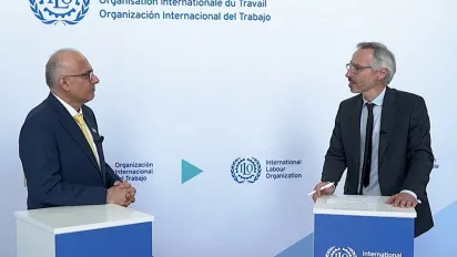 The two men stand facing each other behind podiums bearing the ILO logo, against a backdrop displaying the organization's name in English, French and Spanish.