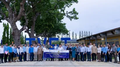 A large group of people stand outdoors in front of a building, gathered around a banner for a group photo.