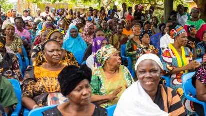 A large group of women, men and young people participate in a community sensitization session focused on health insurance, social protection and child labour prevention.