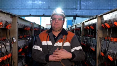 Le mineur Ivan Katolik porte un équipement comprenant une lampe frontale allumée en préparation pour descendre dans une mine de charbon. Il se tient dans une pièce avec des rangées d’équipement de chaque côté de lui.