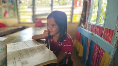 An elementary school girl smiling and reading her book.