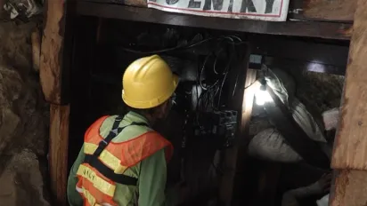 A miner wearing a hard hat and protective gear enters a mining tunnel during a safety inspection.