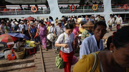 Crowds of people disembark from a passenger ferry at a busy riverside landing
