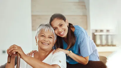 A smiling social worker helping senior woman holding a walking stick in her hand