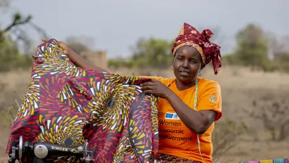 La créatrice de mode zimbabwéenne Martha Simango est assise à l'extérieur, près d'un champ, et brandit l'une de ses créations, une robe multicolore sur laquelle elle travaille.
