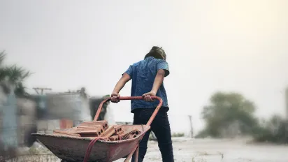 A young male child labourer pulling bricks in a wheel barrow
