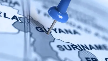 Photo of a blurred map of south america with a blue pin on the map on the location of Guyana