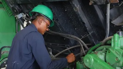 A young man in blue coverall and a green safety helmet repairing an engine 