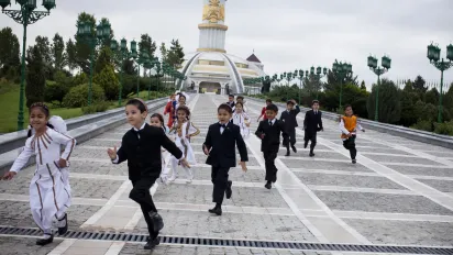Young children in traditional outfits run in front of the Independence Monument of Turkmenistan in Ashgabat, Turkmenistan.