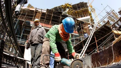 A migrant worker cuts through a metal rod at a construction site.