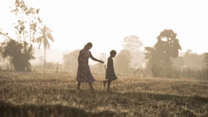mother and young daughter walk amidst a paddy field enveloped by mist