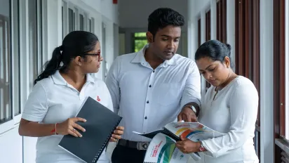A man and 2 women walk along a corridor while examining a training manual book 