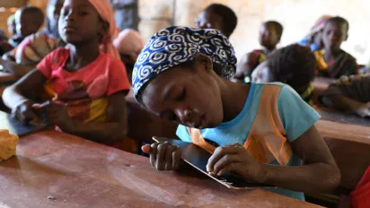 A young girl in school is writing on her slate