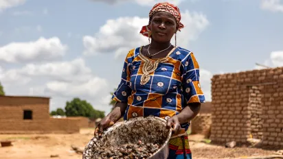 A woman holding a cup containing shea nuts in her village, Mali
