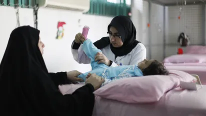 An Iraqi mother holds her child's hand as a nurse examines his leg