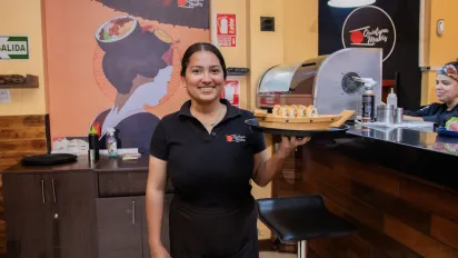 Mujer joven posa con bandeja en mano ante la barra de un restaurante