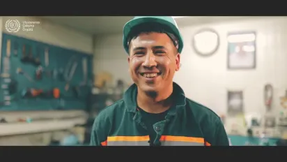 A handy man in green jumper, against a set of tools on a wall, smiling in Turkiye