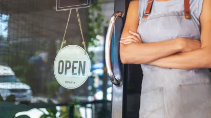 A female waitress wearing an apron standing at the door with a sign Open waiting for customers