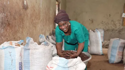 Zakaria Adama Lacera smiles for the camera while scooping up shea butter nuts from a large white sack