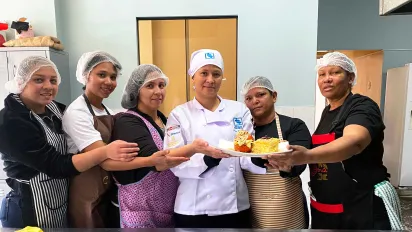 Roxanys Hernández, a Venezuelan migrant in Peru, stands with her team, showing off a plate of pastries.