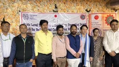 7 men and a woman standing together in front of an ILO event banner