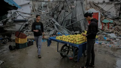 Young man sells oranges in front of a commercial shop destroyed by bombardment in the historic Azzawieh Market in Gaza City.