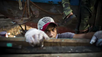 Young worker in a factory wearing gloves and a cap
