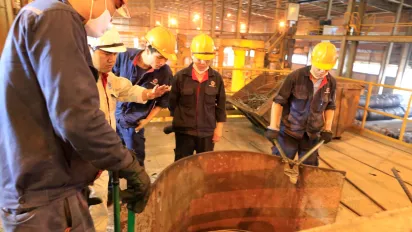 Workers in hard hats with one wearing gloves cut metal sheet with tool.