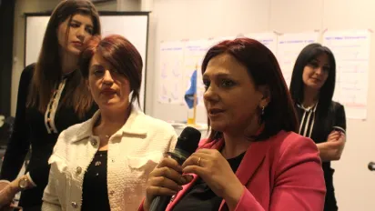 Four women stand in front of the board, one of them holds a microphone