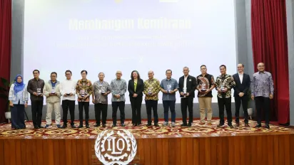 A group photo of 15 people standing on the stage with the ILO logo in font of them.