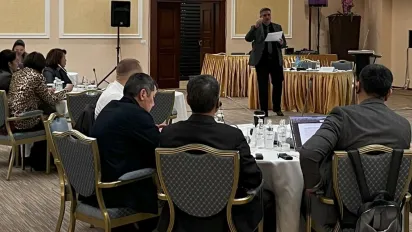 Participants of the OSH seminar sit at round tables and look at the presenter and screen
