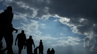 Sun rays illuminate people. Immigration of people. Blue sky with dark clouds.