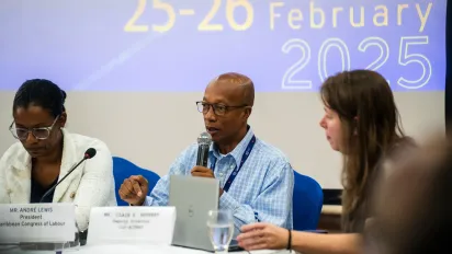Three persons sitting at a table with the man speaking on a microphone