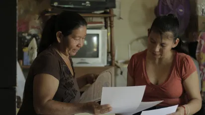 Dos mujeres sentadas en una habitación observando algunos documentos impresos.