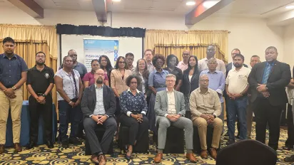 Group photo of approximately 30 participants standing and seated indoors at a professional event. Behind them is a banner displaying the logo of the FAO and the FISH4ACP project. 